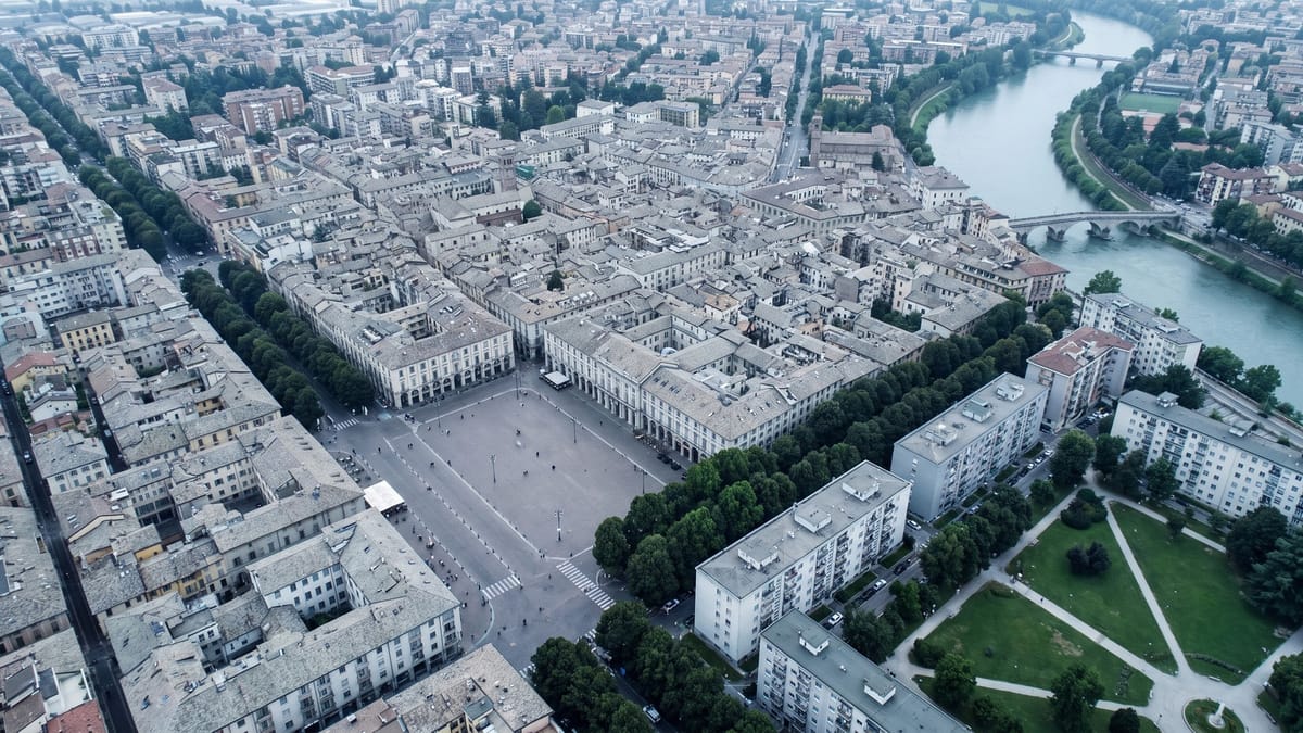 Veduta aerea di una città italiana di media dimensione con tetti, piazza, viali alberati e un fiume