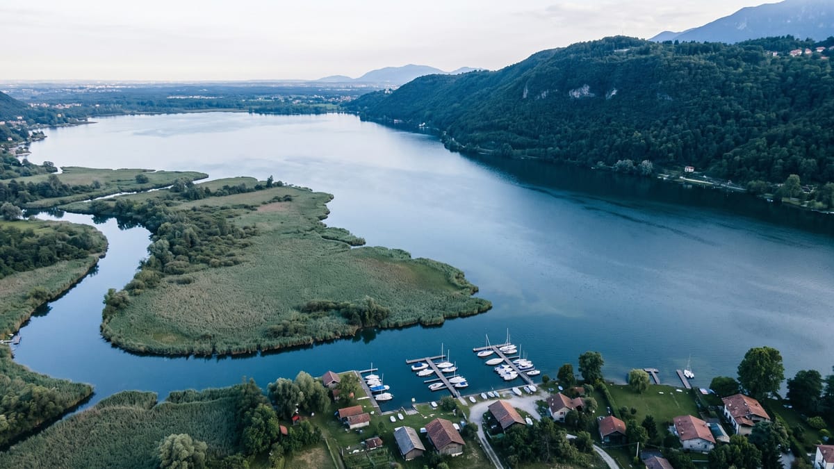 Veduta aerea di un lago prealpino italiano con canneto, foce di un fiume e sponde boscose