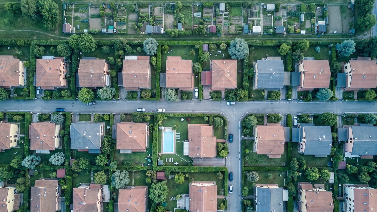 Veduta aerea dall'alto di un quartiere residenziale italiano con case, giardini recintati e una piscina