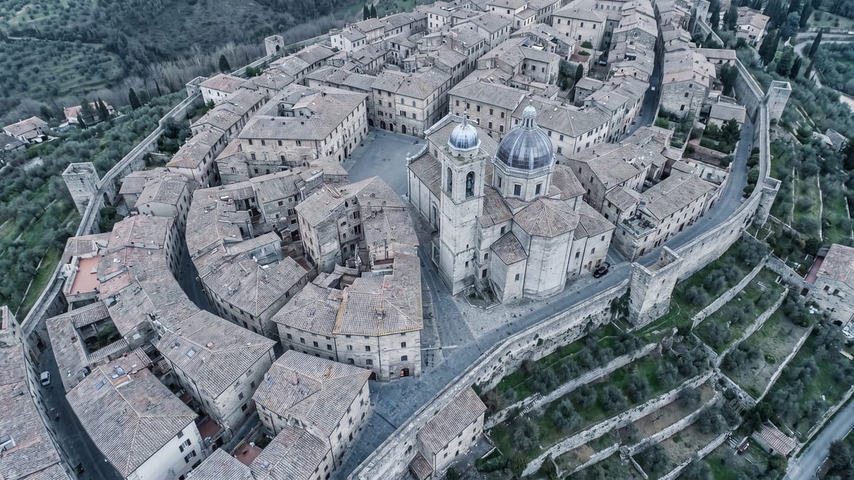 Veduta aerea di un borgo storico italiano con tetti in coppi, cupola, campanile e mura medievali